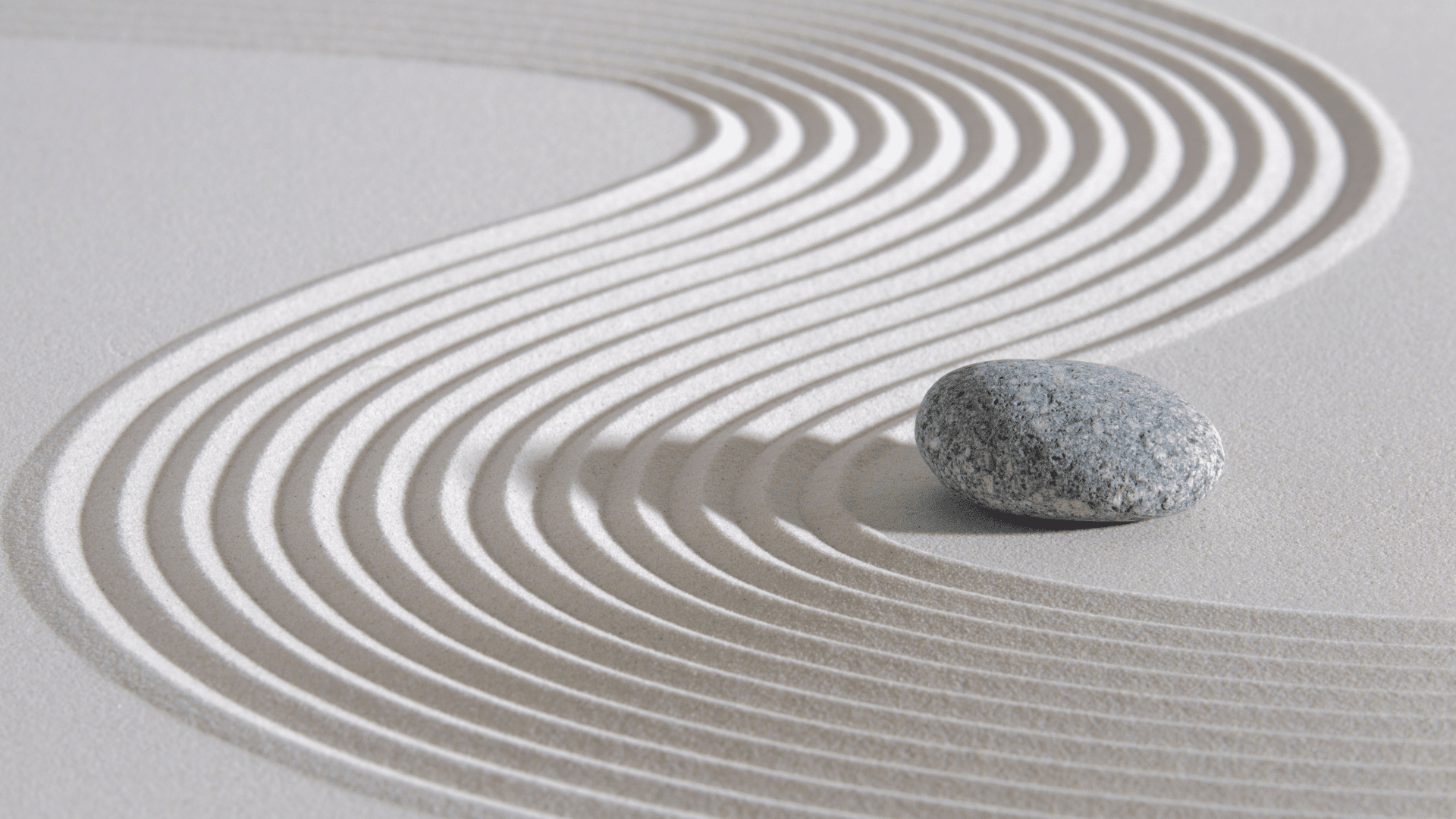 Meditation bei Krebs: ein Stein liegt auf Sand mit geschwungenem Muster