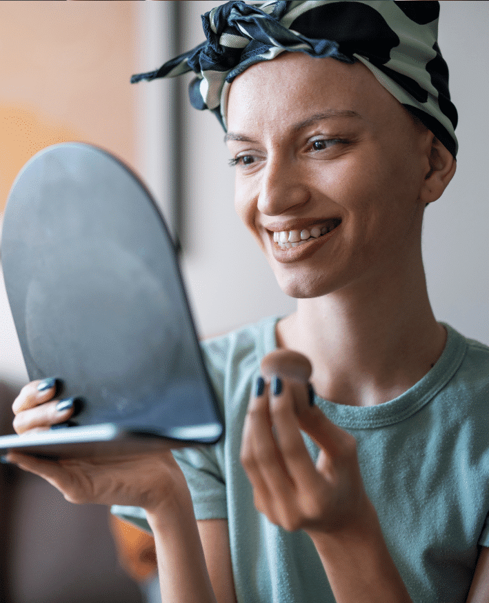 Kosmetik für Krebspatienten: Betroffene mit Krebs lächelt in den Spiegel